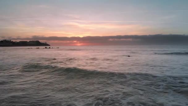 Hava atış. Sunrise okyanus. Pembe ve turuncu renkler. Okyanusu Adası, volkanik taşların lav su dışına taşıyorsa. Palmiyeler ve arka planda birkaç tanınmaz otel vardır. , — Stok video