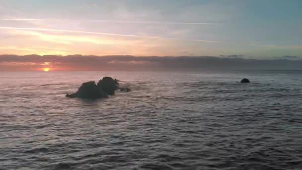 空中ショット。・日の出の海。太陽は地平線の上に登場。ピンクとオレンジの色。海洋島波スプラッシュ水から突き出ている冷凍溶岩の火山石。の — ストック動画