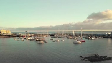 Hava atış. Marina, Atlantik Okyanusu kıyısında küçük bir balıkçı kasabasında bir liman. Çok sayıda tekne, yat ve tekne gün batımında. Volkanik sahile iniş kamerada. Ortasında