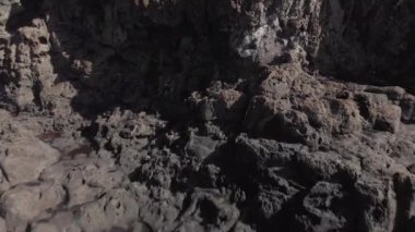 Hava atış. Volkanik yüzey okyanus kıyı şeridi. Koyu gri ve sarı taş yakın çekim. Dolly okyanus dalgalarının Turkuaz rengi vurdu