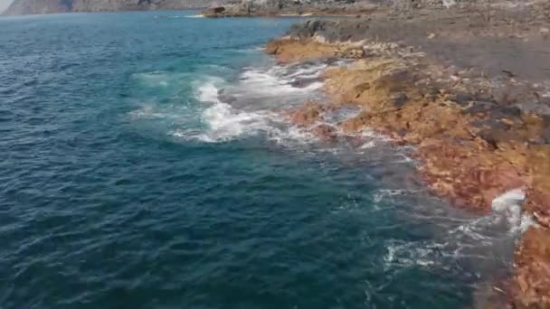 Un disparo aéreo. Plan vertical caído. las olas están salpicando de azul y turquesa en color y la costa volcánica de piedras y lava fósil seca, Sea surf, Tenerife, Islas Canarias, España. Estático — Vídeo de stock