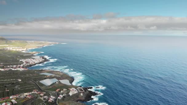 Antenn skott. Lång kustlinje, starka vågor. Blå havet och vulkaniska shore. En liten stad vid stranden av Atlanten, nära basen av bergen. Kaskader av vegetation. Garachico, Teneriffa — Stockvideo