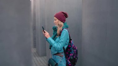 Ağır çekim beyaz kız turist sonbahar Berlin'de merkezi bir sırt çantası ile. Memorial fotoğrafını öldürülen Yahudilerin Avrupa bir smartphone cep telefonu ile yapar. Yalnızlık, kavramı