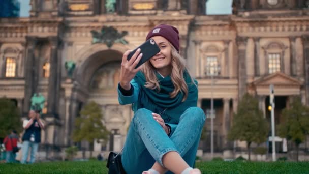 Caucasian tourist girl in the fall makes selfie photo on her smartphone sitting on a lawn near the cathedral in Berlin, Germany. Slow Motion — Stock Video