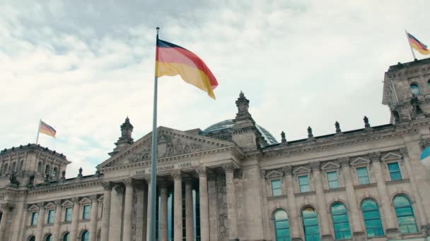 Moción lenta La bandera de Alemania en el contexto del edificio del Bundestag - parlamento en el centro de la capital Berlín. En el fondo del cielo azul y pacífico. Reichstag moderno — Vídeo de stock