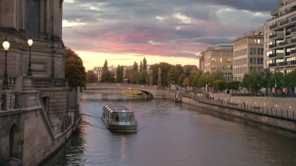 Navio com turistas navegando no rio perto da ilha de museus em Berlim. Pôr do sol no centro da capital. Nuvens multicoloridas rosa. A luz acende-se nas casas. câmara lenta — Vídeo de Stock