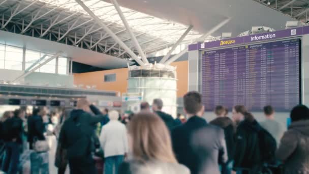 Tablero informativo Slow Motion Enorme en el aeropuerto internacional. A su alrededor hay turistas desconocidos, borrosas y viajeros con maletas. Esperando la salida. Ucrania, Kiev — Vídeo de stock