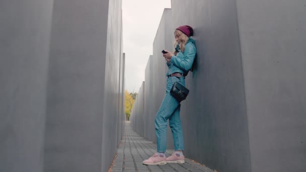 BERLIN, GERMANY - October 2018: Slow Motion Caucasian girl tourist stands clinging on the Murdered Jews of Europe. Uses a mobile phone. writes a message — Stock Video
