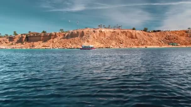遊覧船は海の青い表面で動く。岩の海岸とビーチの背景に対して黄色です。楽園での休息の概念。スローモーション — ストック動画