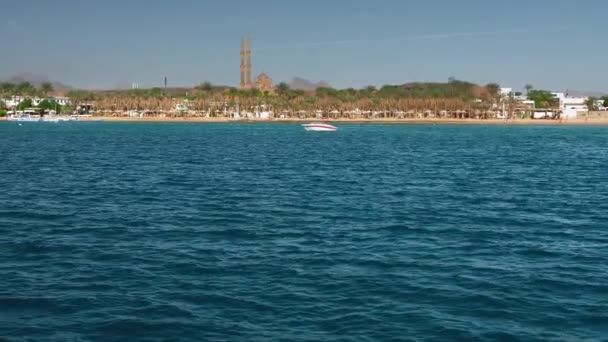 Turistický vysokorychlostní člun na pozadí modrého moře a pobřeží palmových stromů. V dálce se nachází velká Arabská muslimská mešita a dvě minarety. Zpomaleně — Stock video