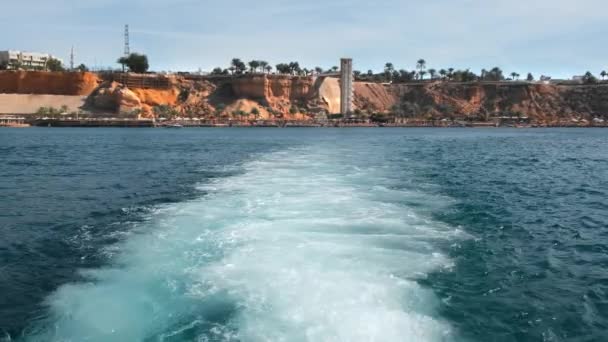 Nachverfolgung nach der Passage einer Yacht oder eines Schiffes auf dem Wasser. weißer Meeresschaum aus dem Motor des Schiffes. vor dem Hintergrund einer felsigen Klippe die Küste einer tropischen Insel. das Konzept des Endes — Stockvideo