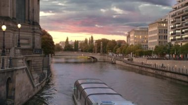 Berlin'deki müzeler adası yakınlarındaki nehirde seyreden turist gemileri. Tanışın ve farklı yönlere yüzebilirsiniz. Başkentin merkezinde gün batımı. Pembe çok renkli bulutlar. Işık yanar