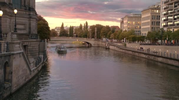 Barco de recreio flutua no rio perto da ilha de museus em Berlim. Pôr do sol no centro da capital. Nuvens multicoloridas rosa. A luz acende-se nas casas. câmara lenta — Vídeo de Stock