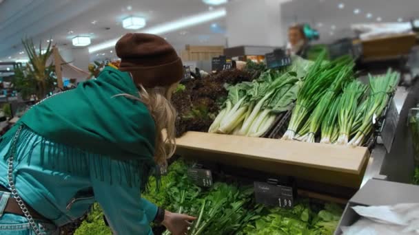 Gyönyörű kaukázusi lány egy kék kabát és egy zöld sálat, dönt és vásárol zöld zöldségek és egészséges termékek a szupermarketben. A koncepció az egészséges táplálkozás és a túlsúly, lassított