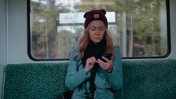 Jeune fille caucasienne aux yeux bleus monte dans un métro ou un tramway, utilise le téléphone, imprime un message et regarde autour de lui. Mouvement lent — Video