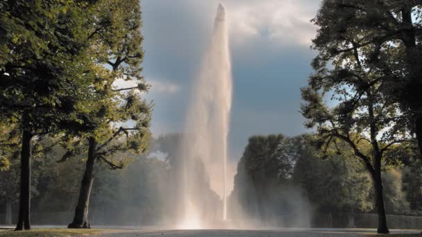 Ганновер, Германия. Высокая струя воды из фонтана, извергающаяся из чаши, установленной на земле под заходящим солнцем. На фоне зеленых деревьев в парке. Концепция сохранения природы — стоковое видео