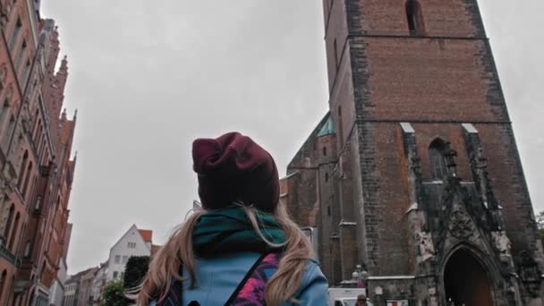 Menina turística com uma mochila explorando e considerando a visão. Antiga igreja-capela católica de tijolo vermelho. Alemanha, Hanôver. Movimento lento — Vídeo de Stock