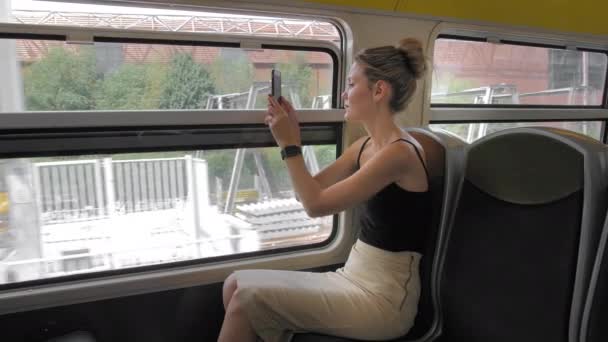 美しい白人女性観光客は電車に乗り、市内の工業地帯の写真を撮ります。窓の倉庫や他の構造で。スローモーション — ストック動画