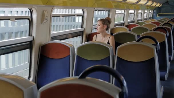 Una hermosa turista caucásica viaja sola en un tren subterráneo de cabina vacía y mira por la ventana. Detrás de ella hay filas vacías de asientos. El concepto de soledad. Moción lenta — Vídeos de Stock