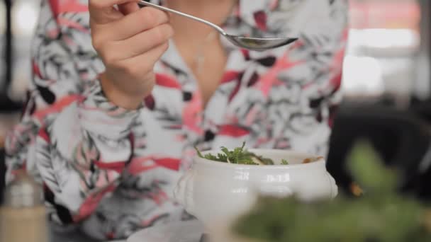 Eine unbekannte Touristin in einem bunten Hemdlöffel isst in einem Pariser Restaurant eine traditionelle französische Zwiebelsuppe mit Croutons, geschmolzenem Käse und Kräutern. Nahaufnahme, Zeitlupe — Stockvideo