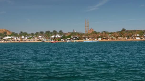 在夏天的阳光明媚的一天，在蓝色美丽的海面上移动快艇。以棕榈树和度假村酒店为背景。远处可以看到一座尖塔和一座清真寺。慢动作 — 图库视频影像