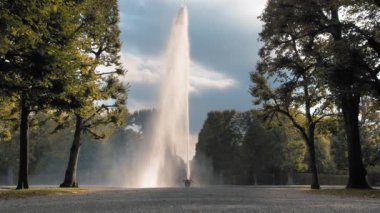 Hannover, Almanya. Büyük, yüksek Jet Su Çeşmesi yere yerleştirilen bir kase dışarı dökülen. Parkta yeşil ağaçların arka plana karşı. Yavaş hareket