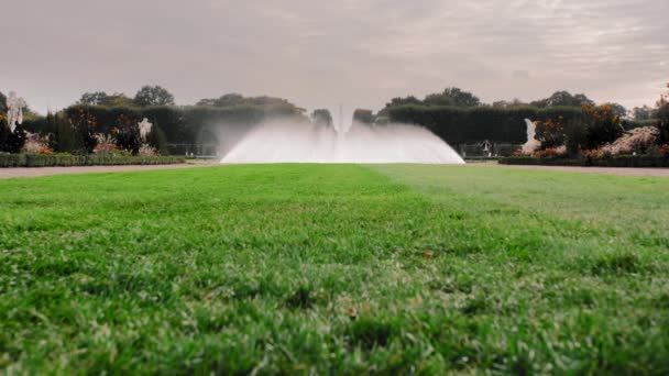 Hannover, Německo. Velká fontána v zahradě se stříkající vodou. V popředí je zelený trávník s trávou. V dálce se z neznámých turistických fotografií nachází orientační bod. Zpomaleně — Stock video