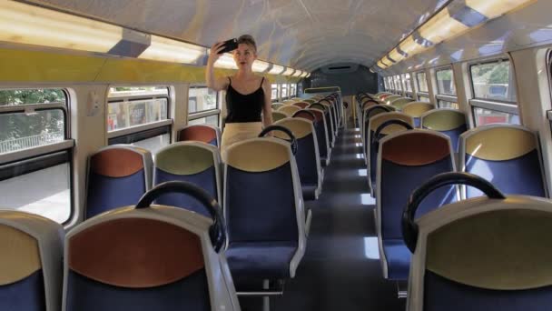 Красивая кавказская туристка в одиночку делает селфи в пустом салоне поезда метро, который находится на станции. За ней пустые ряды сидений. Slow Motion — стоковое видео