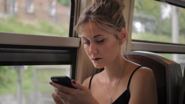 Schöne kaukasische Touristin sitzt im Zug am Bahnhof. verwendet ein Mobiltelefon druckt eine Nachricht und traurig. Zeitlupe — Stockvideo