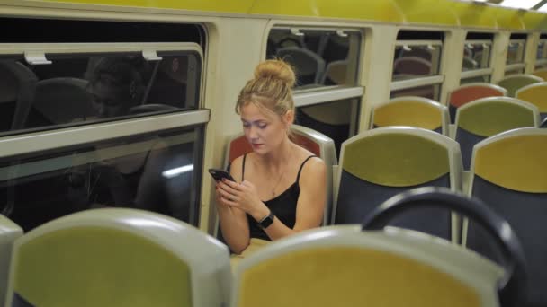 Beautiful Caucasian female tourist rides in an empty train through a dark tunnel. behind the rows of seats, lights are moving outside the window. Uses mobile phone prints message. shes sad. Hair — Stock Video