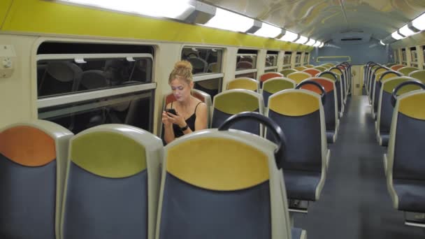 Belle balade touristique féminine caucasienne dans un train vide en deux étapes à travers un tunnel sombre. derrière les rangées vides de sièges, lumières se déplaçant à l'extérieur de la fenêtre. Utilise le message d'empreintes de téléphone mobile. shes — Video