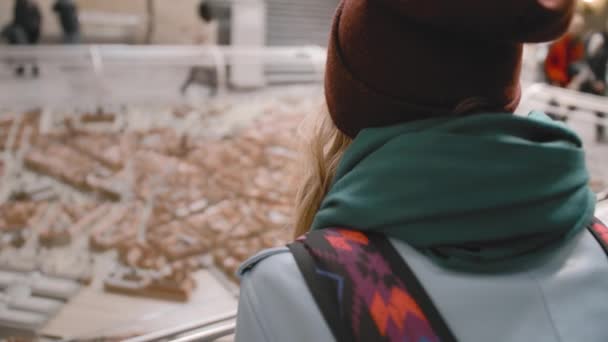 Jonge vrouwelijke toerist met een rugzak op haar schouders onderzoekt een miniatuur installatie van de stad met huizen en straten. Langzame beweging — Stockvideo