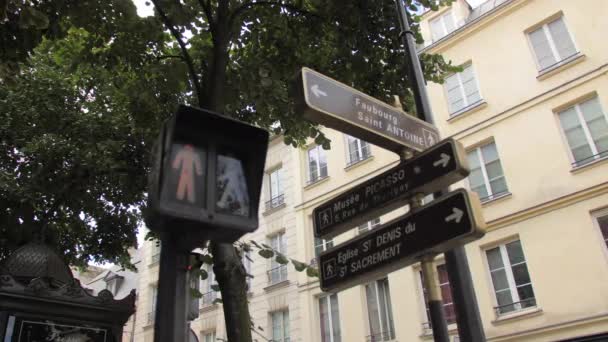 Париж, Франція-Серпень 2018: перемикання світла від червоного до зеленого на пішохідних світлофорів. У каркасі таблички на будиночки, вуличні вивіски. Гілочки зелених дерев. Концепція дозволу на переміщення — стокове відео