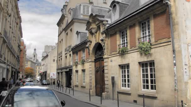 Париж, Франція-Серпень 2018: типова вулиця в центрі Старого міста. Є пішоходи ходьбі, квіти ростуть на вікнах. На передньому плані знаходиться старий будинок з великими вінтажними дверима — стокове відео