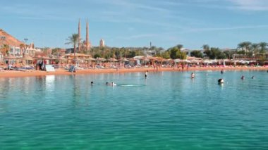 küçük çocuk şişme bir daire ile denizde yüzer. Güzel lüks bir tatil köyü. Turkuaz su ile plaj kumlu deniz kıyısı. Turistler rahatlar, yüzer ve bronzlaşmak. Yüzmeyi öğrenme kavramı. Yavaş Çekim
