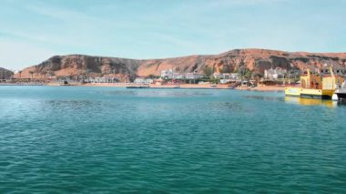 Tropik manzara mavi, turkuaz deniz, çöl dağlarının sarı kıyılarına karşı. Palmiye ağaçları, plaj ve dinlenme ve rahatlama için oteller. Yatlar ve tekneler kıyıya yakın demirler. Alınan bir