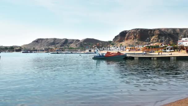 Ο θαλάσσιος κόλπος σε μια τροπική πόλη. αρκετές βάρκες, μια παραλία με τουρίστες και φοίνικες. Όμορφο γαλάζιο νερό. Αργή κίνηση — Αρχείο Βίντεο