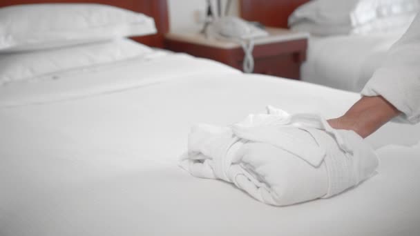 Eine unerkannte erwachsene Seniorin nimmt einen weißen Mantel, der auf einem Bett in einem Hotelzimmer liegt. das Konzept von Service und Reinigung im Hotel. Zeitlupe — Stockvideo