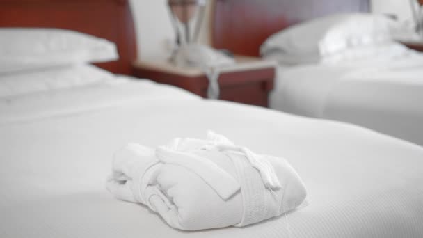認識されていない大人のシニア女性は、ホテルの部屋のベッドの上に白いバスローブの隣に完全に白いタオルを置き、まっすぐにします。スローモーション、クローズアップ — ストック動画