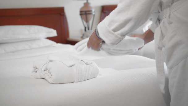 Seorang wanita senior dewasa yang tidak dikenal menempatkan handuk putih di samping jubah mandi putih di tempat tidur di kamar hotel. Gerakan Lambat, Pendekatan — Stok Video