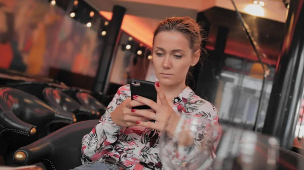 Joven francesa utiliza las redes sociales para comunicarse con un teléfono móvil. Se sienta en un restaurante a la espera de su pedido. Moción lenta —  Fotos de Stock