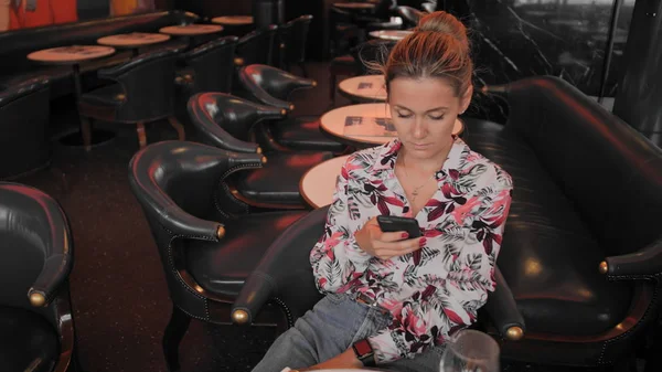Joven francesa utiliza las redes sociales para comunicarse con un teléfono móvil. En el fondo de una sala vacía en el restaurante. Disparo de muñeca de cámara lenta —  Fotos de Stock