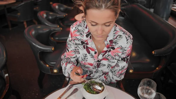 Belle Française en chemise panachée mange une soupe à l'oignon française traditionnelle avec croûtons et légumes verts dans un restaurant. Mouvement lent Image En Vente