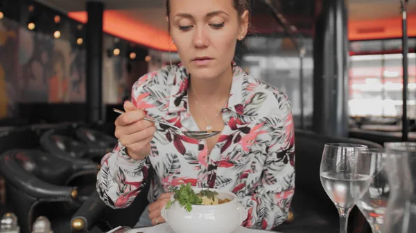 Belle touriste féminine dans une cuillère à chemise colorée mange une soupe à l'oignon française traditionnelle avec croûtons et légumes verts dans un restaurant parisien. Mouvement lent Image En Vente