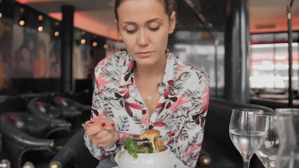Belle touriste féminine dans une cuillère à chemise colorée mange de la soupe traditionnelle aux oignons français avec croûtons, fromage fondu et herbes dans un restaurant parisien. Mouvement lent Photo De Stock
