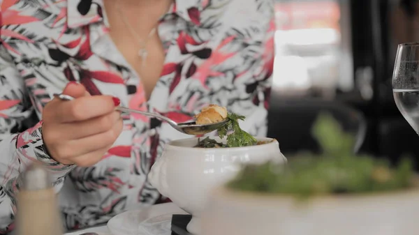 Une touriste non reconnue mange de la soupe traditionnelle avec croûtons, fromage fondu et légumes verts dans un restaurant parisien. La main prend une branche d'aneth. Le concept de mauvaise étiquette. Gros plan, ralenti Photo De Stock