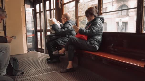 Milan, Italie - Mai 2019 : Un Italien âgé et une jeune femme asiatique montent dans un tramway rétro milanais. Un homme lit un journal, une femme utilise un smartphone. Le concept d'obtention d'informations auprès de la — Video