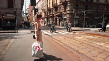 Milano, İtalya - Mayıs 2019: Güzel genç Beyaz kadın alışveriş ten sonra bir çanta ile şehir merkezinde bir kavşakta duruyor. Yavaş çekim