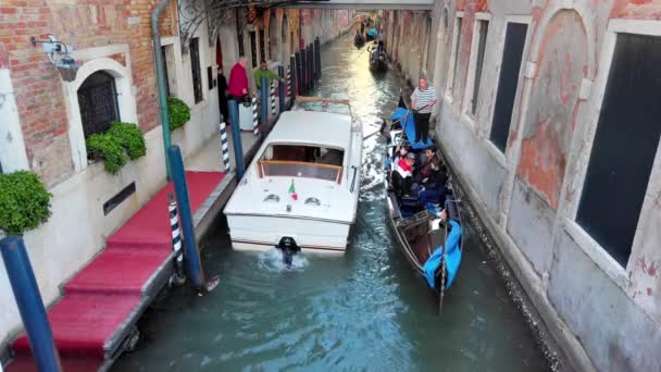 Venetië, Italië-mei 2019: passagiers instappen in de buurt van het Hotel in een luxe taxi boot in het smalle kanaal van Venetië. Doorman helpt bij het laden van bagage. In de omgeving is een gondel met toeristen uit Azië. Langzaam — Stockvideo