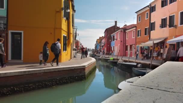 Burano, Βενετία, Ιταλία-2019 Μαΐου: οι άνθρωποι περπατούν κατά μήκος των στενών βενετσιάνικων δρόμων κατά μήκος του καναλιού. Πολλά σκάφη παρκαρισμένο κοντά στην ακτή. Πολύχρωμα σπίτια του νησιού Burano. Αργή κίνηση — Αρχείο Βίντεο